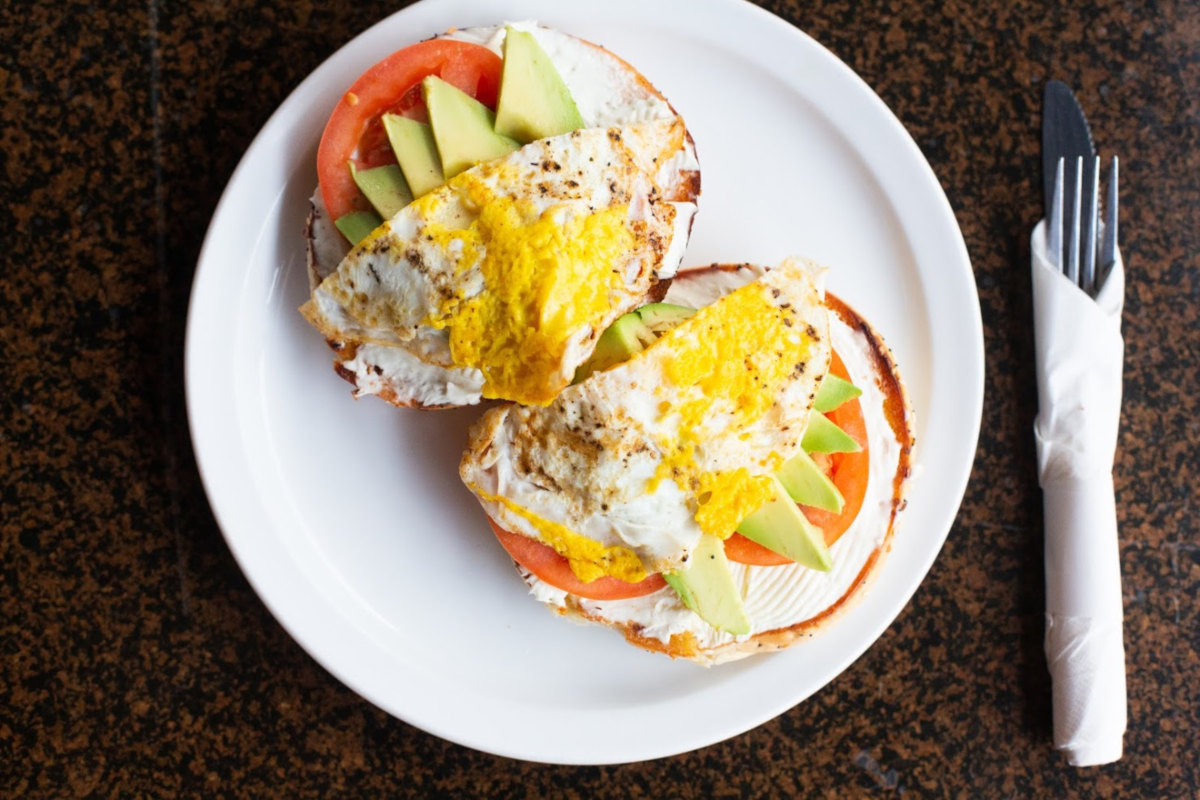 Two sandwiches with white cream, tomato, cucumber, yellow spices on top